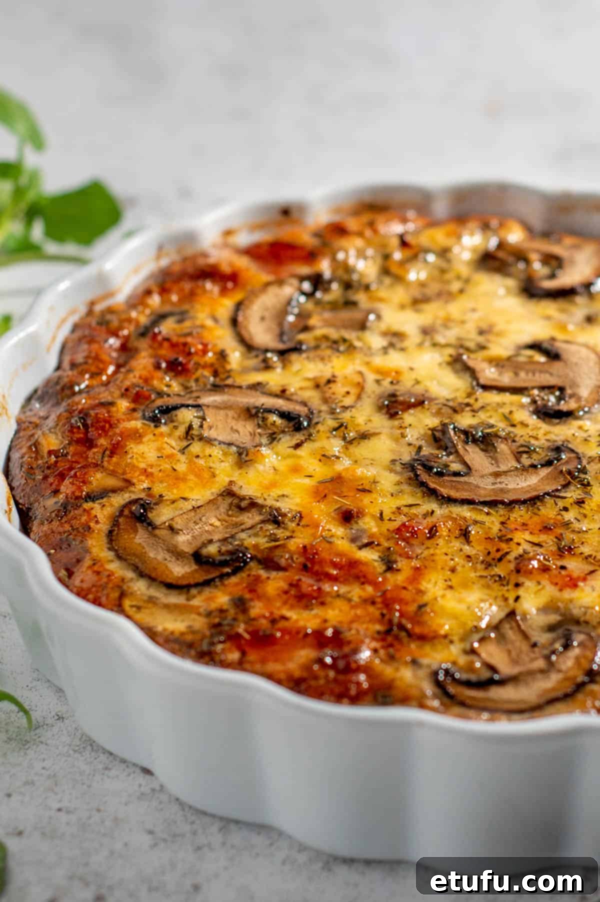 Golden-brown crustless bacon and mushroom quiche in a pristine white tart dish, ready to be served.