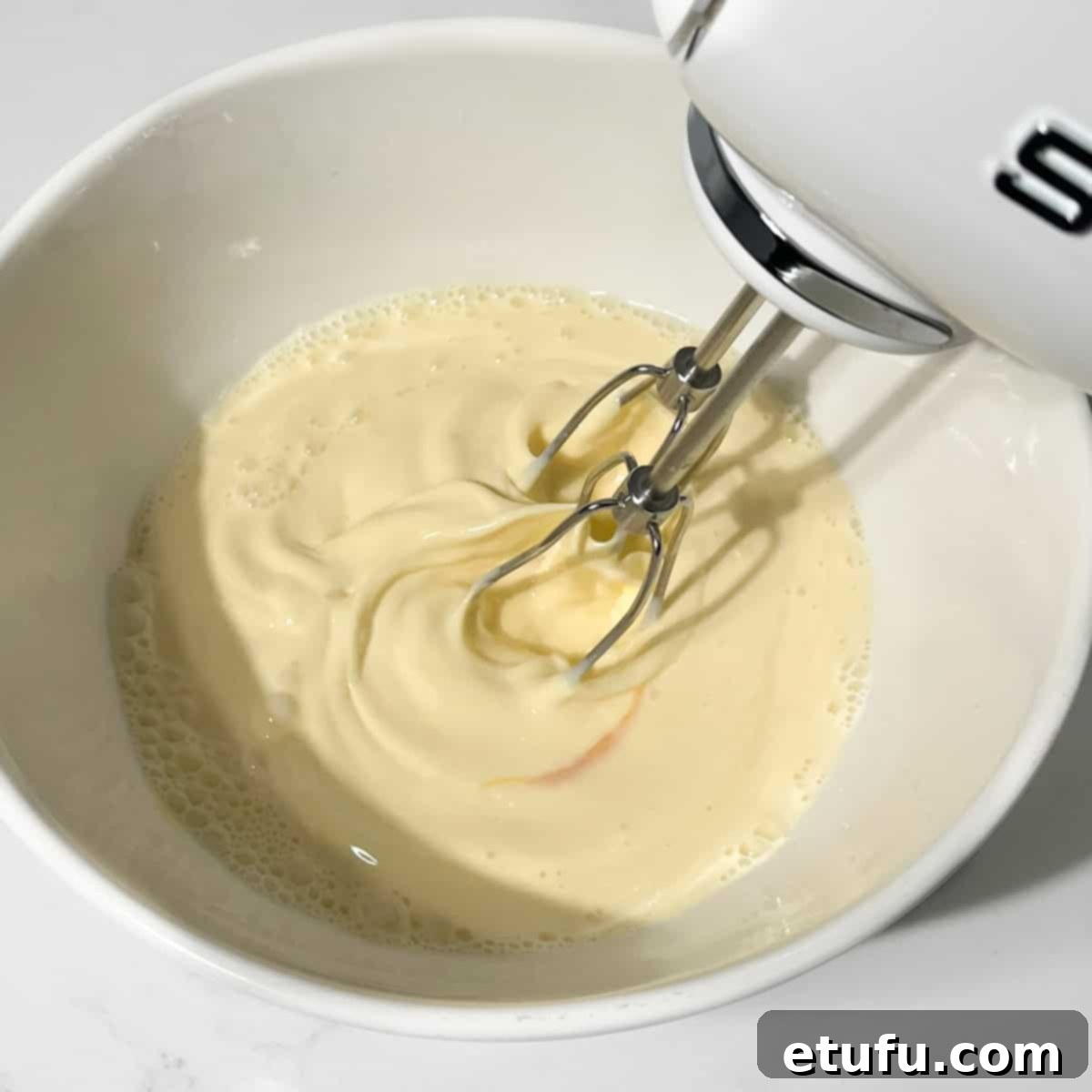 Whisking eggs, milk, cream, and Dijon mustard in a large white mixing bowl.