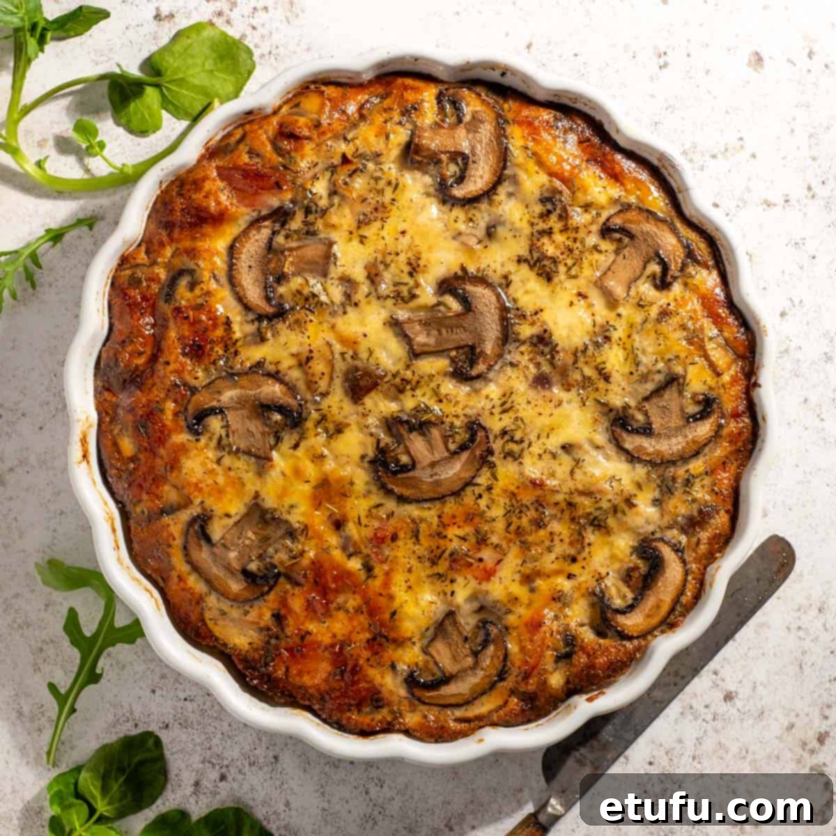 Freshly baked golden-brown crustless bacon and mushroom quiche in a white tart dish, cooling on a wire rack.