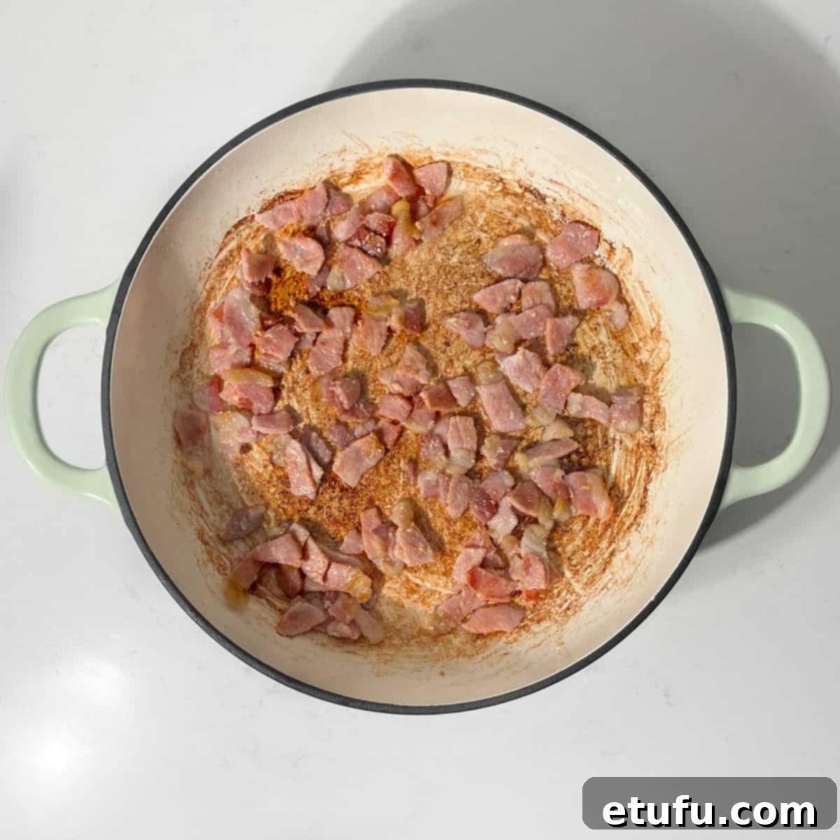 Sizzling diced bacon frying in a large pan, browning to perfection for the quiche.