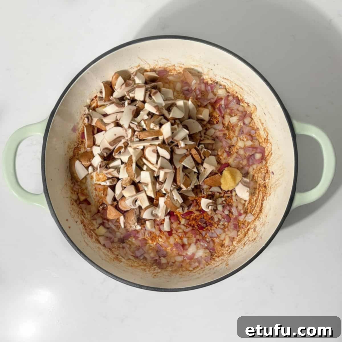 Diced mushrooms added to sautéed onions in a frying pan, beginning to brown.