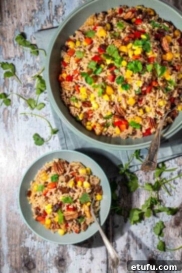 A large bowl of vibrant brown rice salad, with a smaller bowl of dressing or extra ingredients next to it.