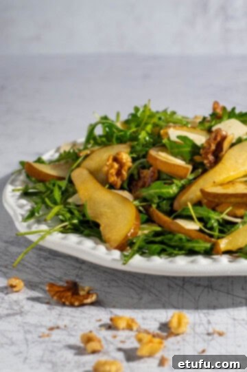 Caramelised pear and rocket salad elegantly arranged on a large white plate.