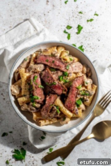 A beautifully presented bowl of creamy steak pasta, garnished with fresh herbs, showcasing tender steak slices, rich mushroom and whisky sauce, and perfectly cooked pasta.