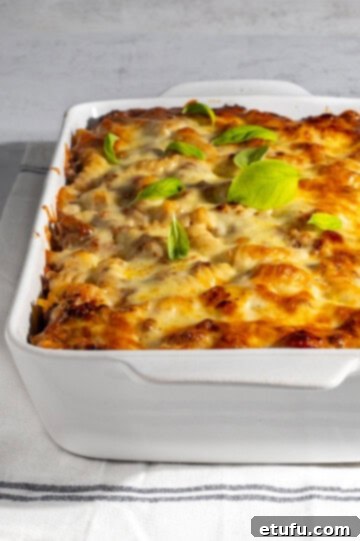 A large rectangular baking dish filled with a golden-brown Bolognese pasta bake, showing rich layers of pasta, meat sauce, béchamel, and perfectly melted cheese.