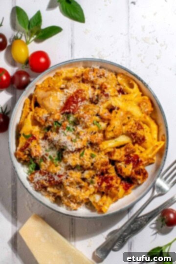 A white bowl brimming with creamy chicken and chorizo pasta, showcasing the vibrant colors of sliced chorizo, tender chicken pieces, sun-dried tomatoes, and a rich, creamy sauce on a white washed background.