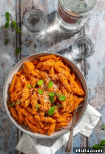 Gigi Hadid's spicy vodka pasta served in a stylish white bowl, richly coated in a creamy, reddish sauce, with a small bottle of vodka visible in the background, hinting at the key ingredient.
