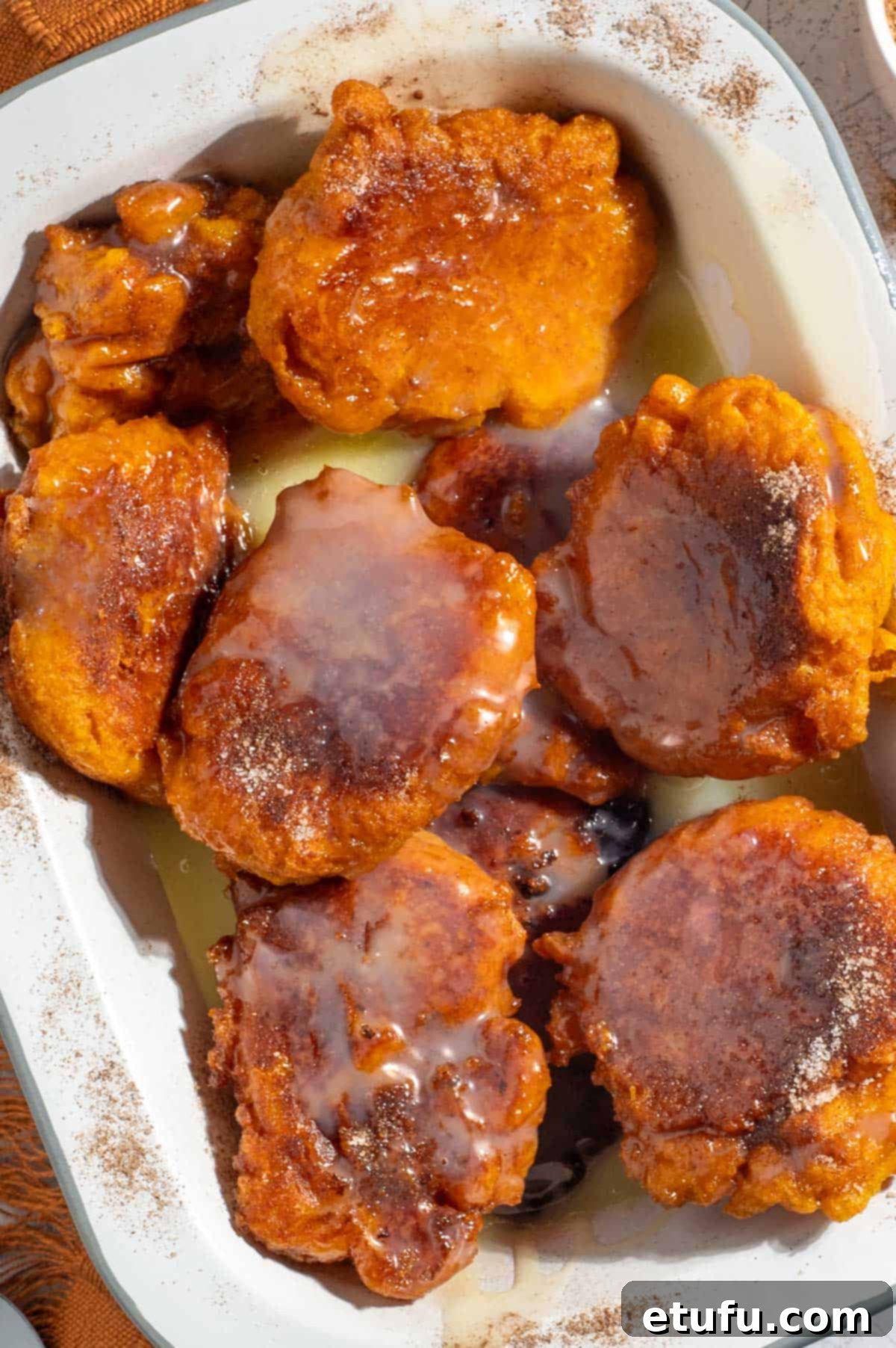 Golden pumpkin fritters (pampoenkoekies) drenched in caramel sauce, served in a rectangular enamel dish, ready to be enjoyed as a sweet side or dessert.