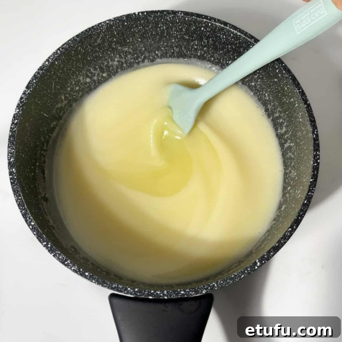 The thickened caramel sauce for pampoenkoekies (pumpkin fritters) simmering gently in a small black saucepan, showing its creamy, pale yellow vanilla color.