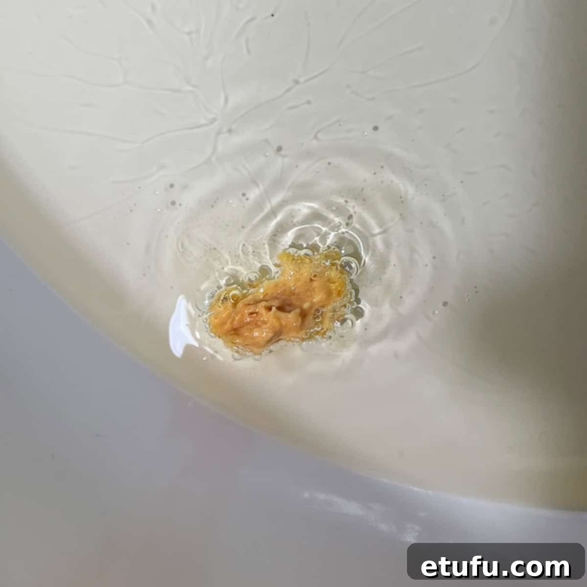 A small piece of pumpkin fritter batter dropped into hot oil in a frying pan, showing rapid, small bubbles forming around it, indicating the oil is at the correct temperature for frying.