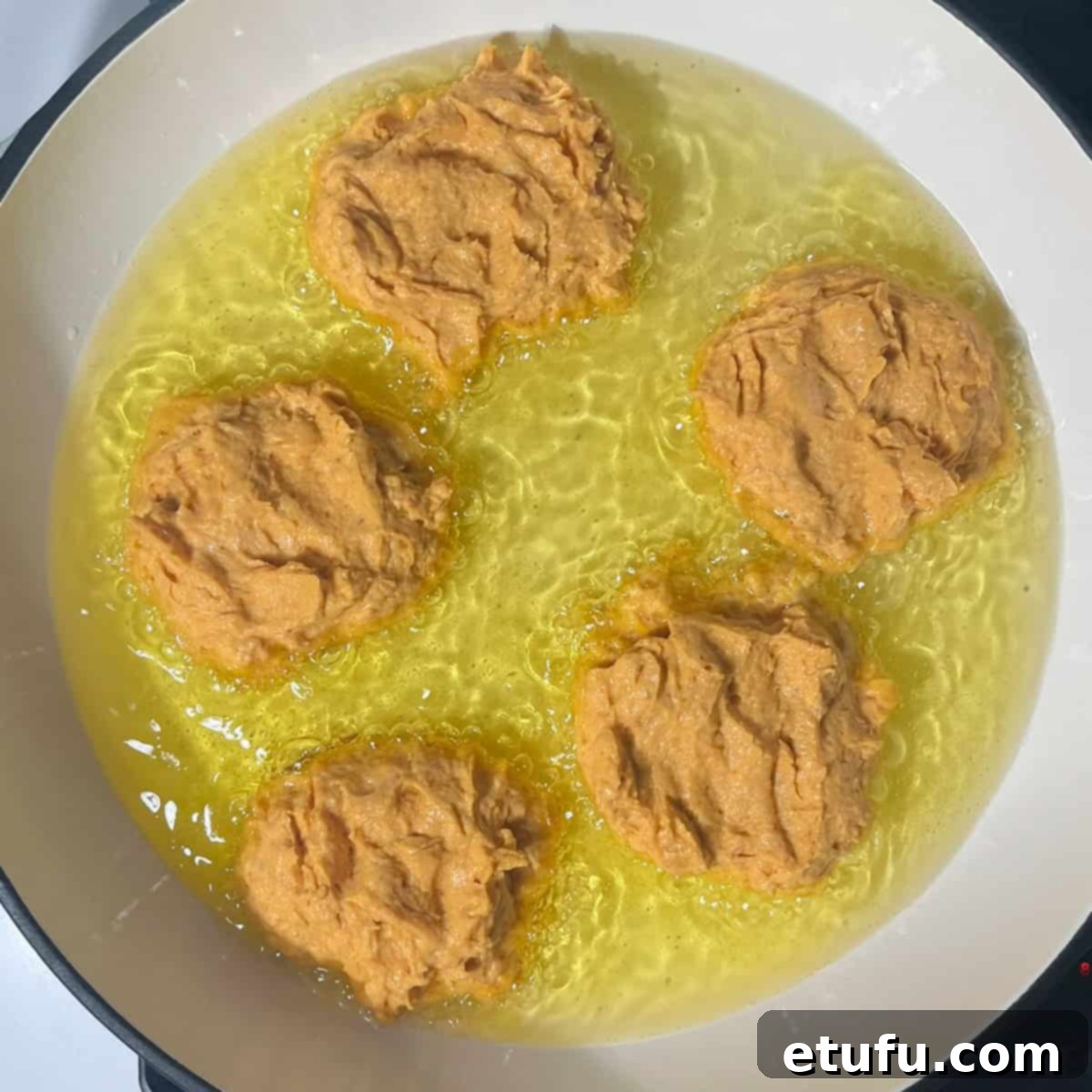 Golden pumpkin fritters (pampoenkoekies) shallow-frying in hot oil in a large pan, cooking to a beautiful dark golden brown.