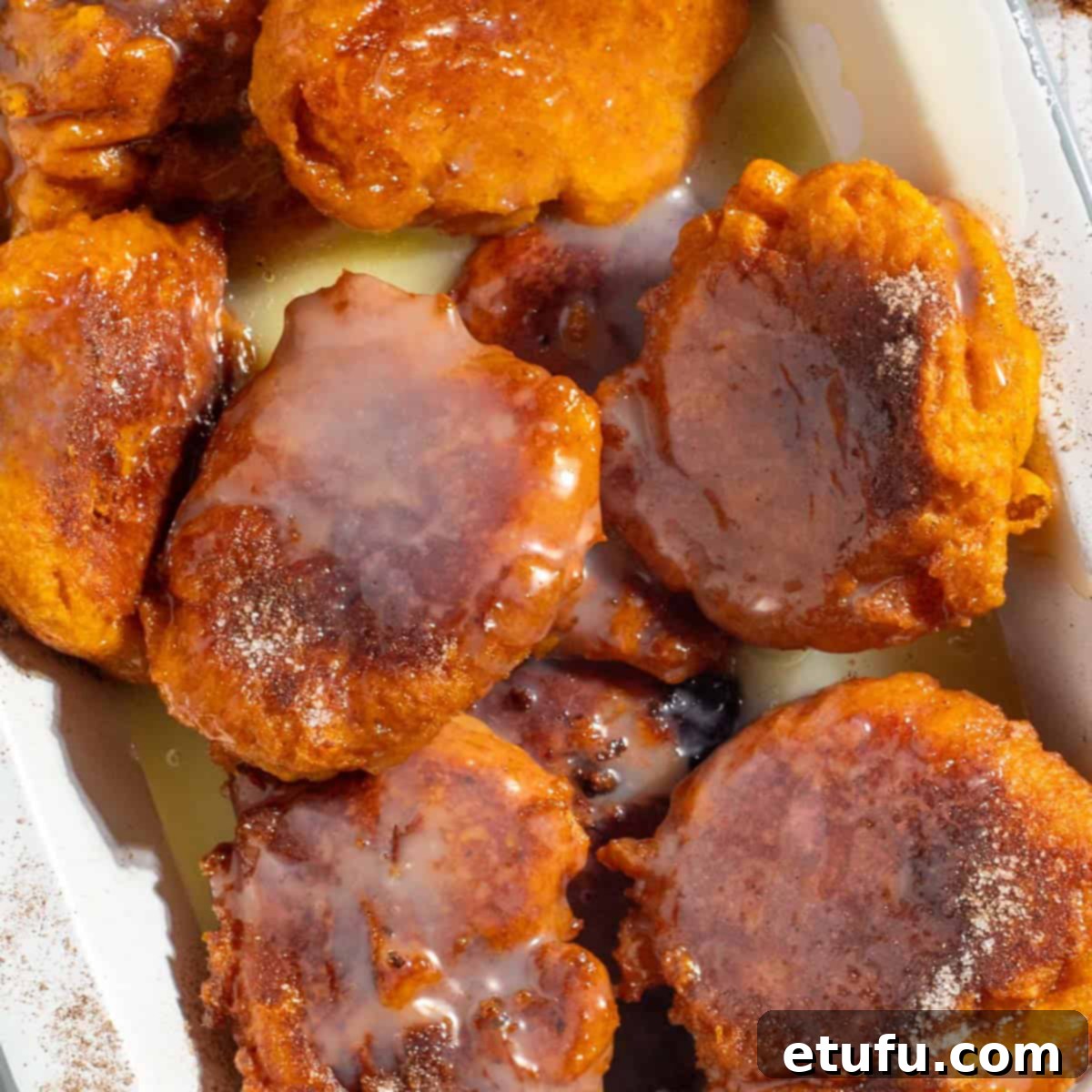 Finished pumpkin fritters (pampoenkoekies) generously drizzled with warm caramel sauce, arranged in a rectangular enamel serving dish, ready to be enjoyed.