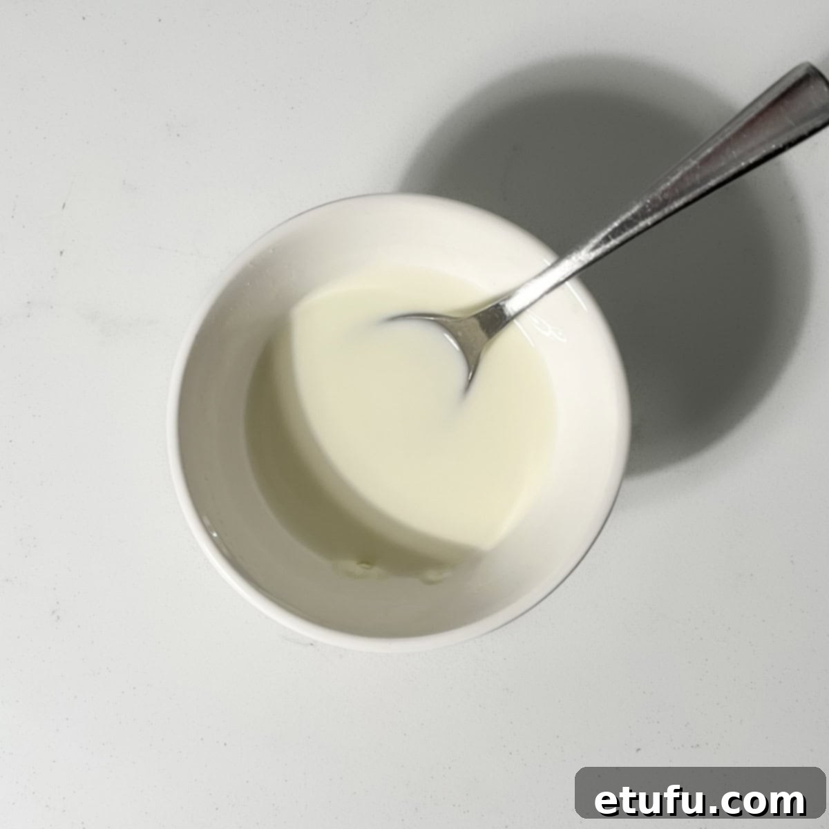 A small white bowl containing cornstarch and water, being stirred to create a smooth slurry, an essential first step for thickening the caramel sauce.