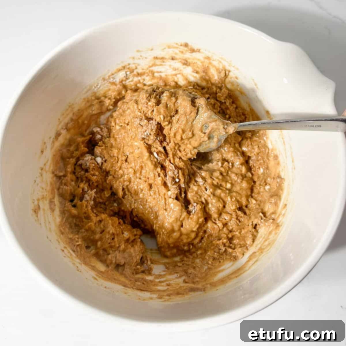 Gently folding the wet ingredients into the dry ingredients in a large white bowl.
