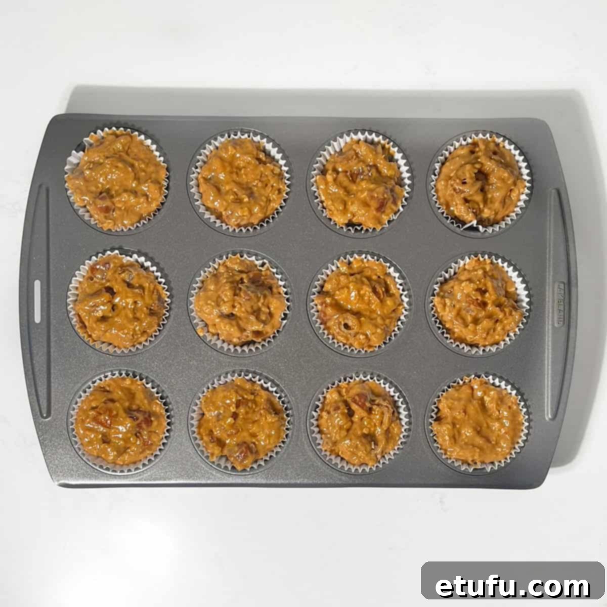 Muffin batter scooped into 12 paper liners in a muffin pan, filled to the brim.
