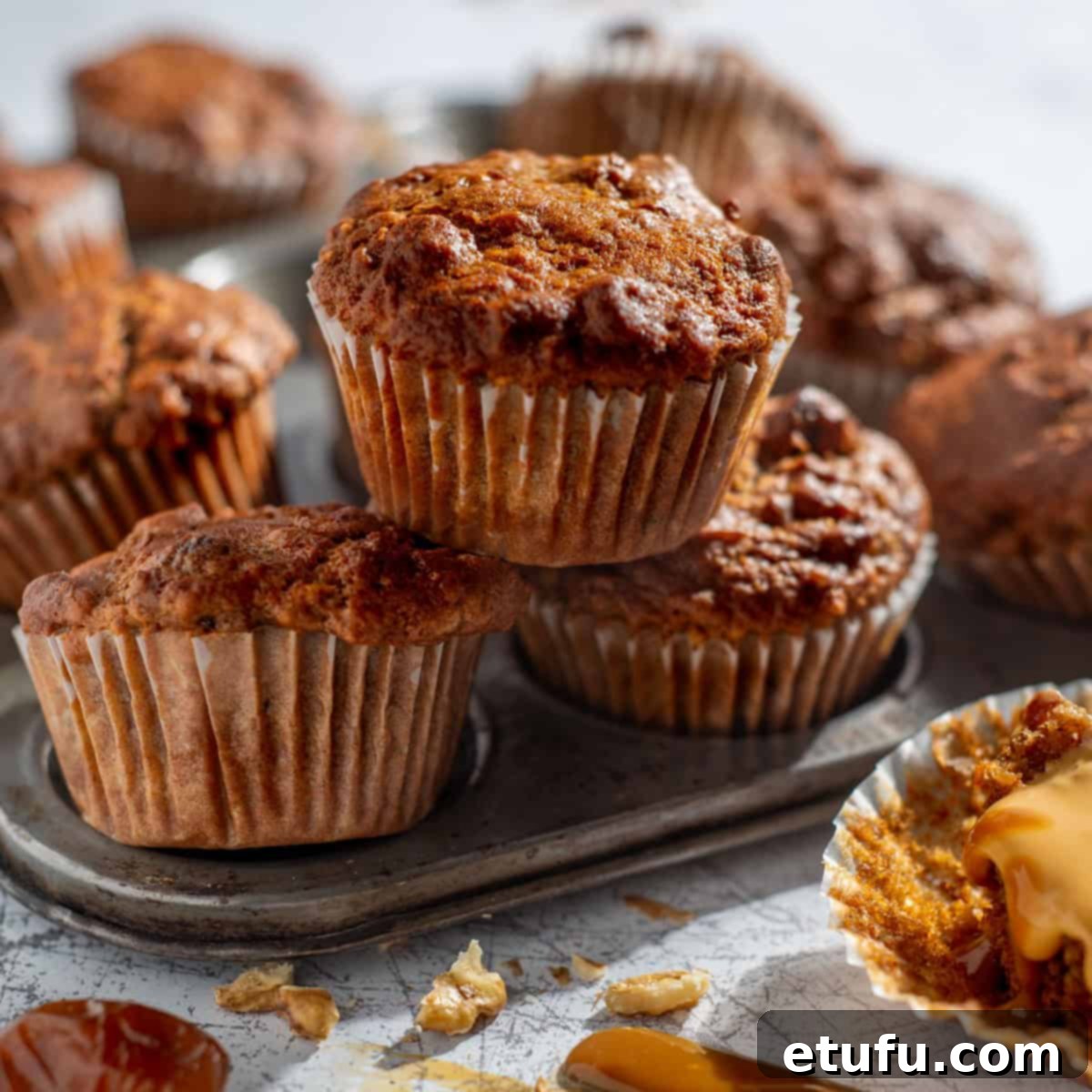 Date muffins in a muffin baking tray with caramel spread on one, ready for serving.
