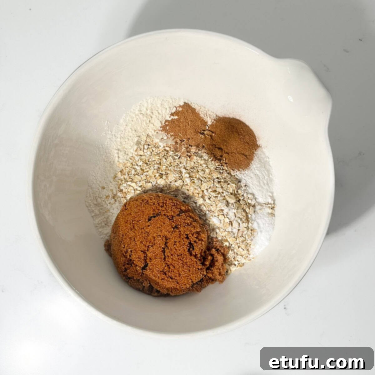 Dry ingredients for date and oat muffins being added to a large white mixing bowl.