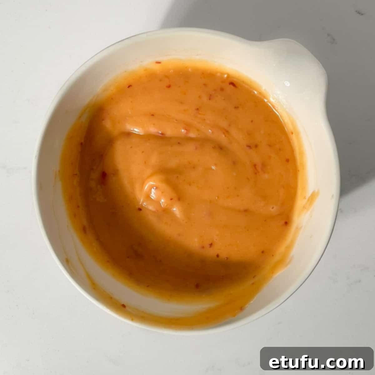 A small white bowl filled with creamy, orange-hued bang bang sauce, ready for serving.