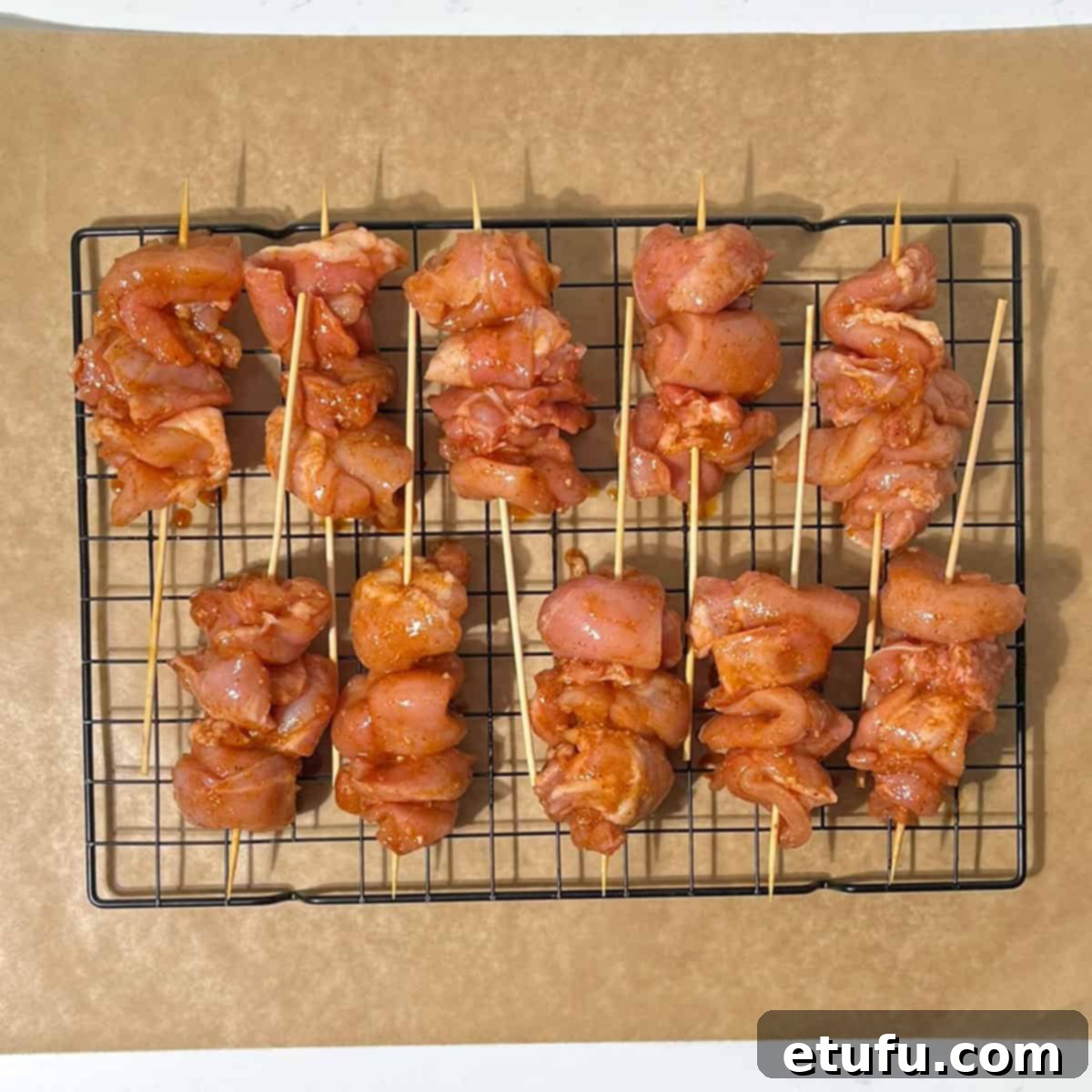 Raw bang bang chicken pieces neatly threaded onto wooden skewers, resting on a wire rack over a baking sheet.