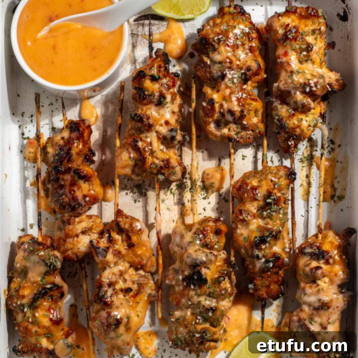 Succulent bang bang chicken skewers, garnished with fresh lime wedges and cilantro, ready to be served alongside a small bowl of dipping sauce.