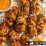 Bang bang chicken skewers on a white background with a small pot of bang bang sauce and lime wedges.