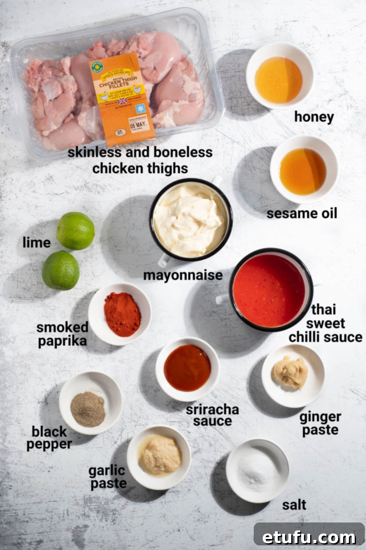 A vibrant selection of ingredients laid out, featuring cubed chicken thighs, various sauces, fresh garlic and ginger, lime, and spices, all ready for making bang bang chicken skewers.