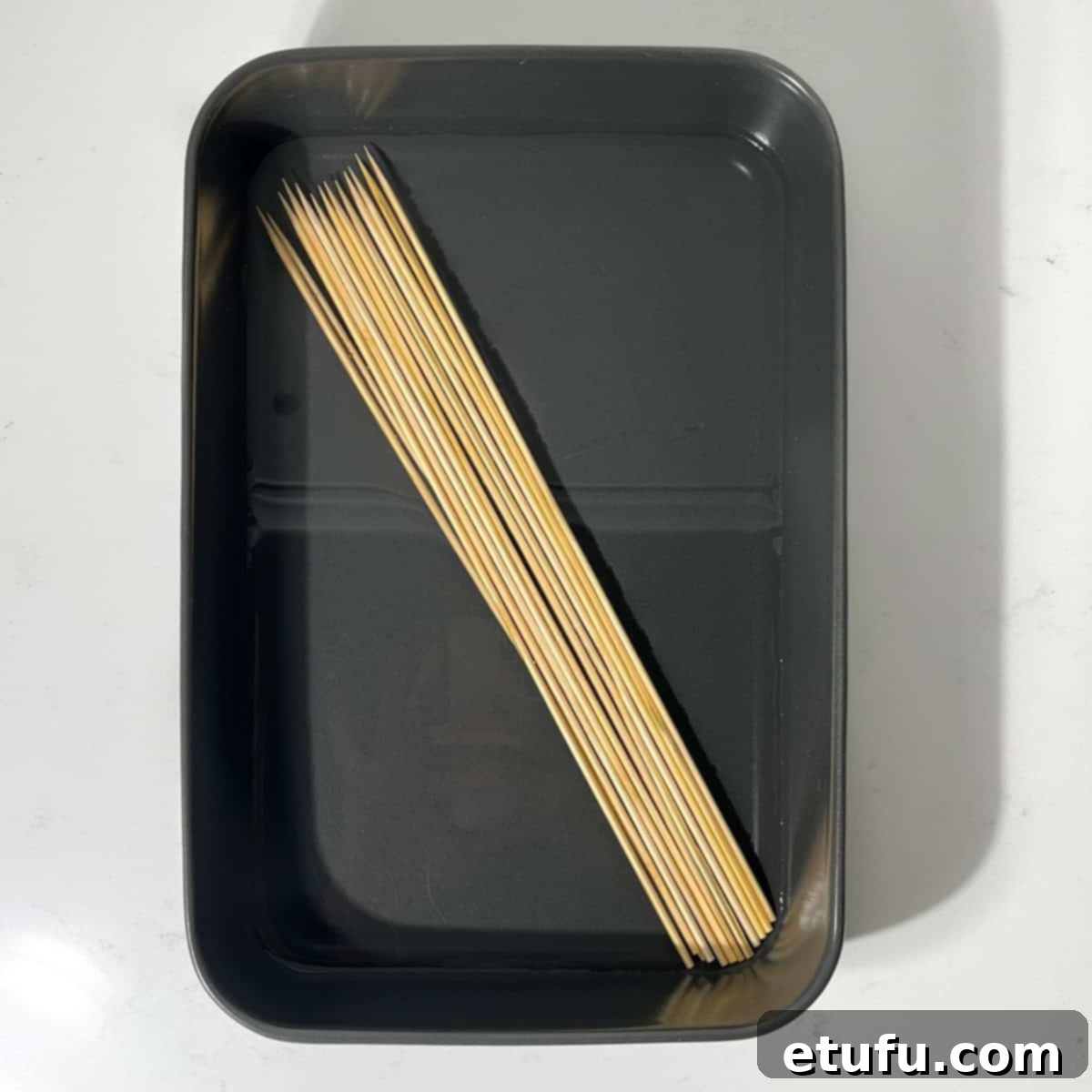 Wooden skewers soaking in a clear glass dish filled with water.