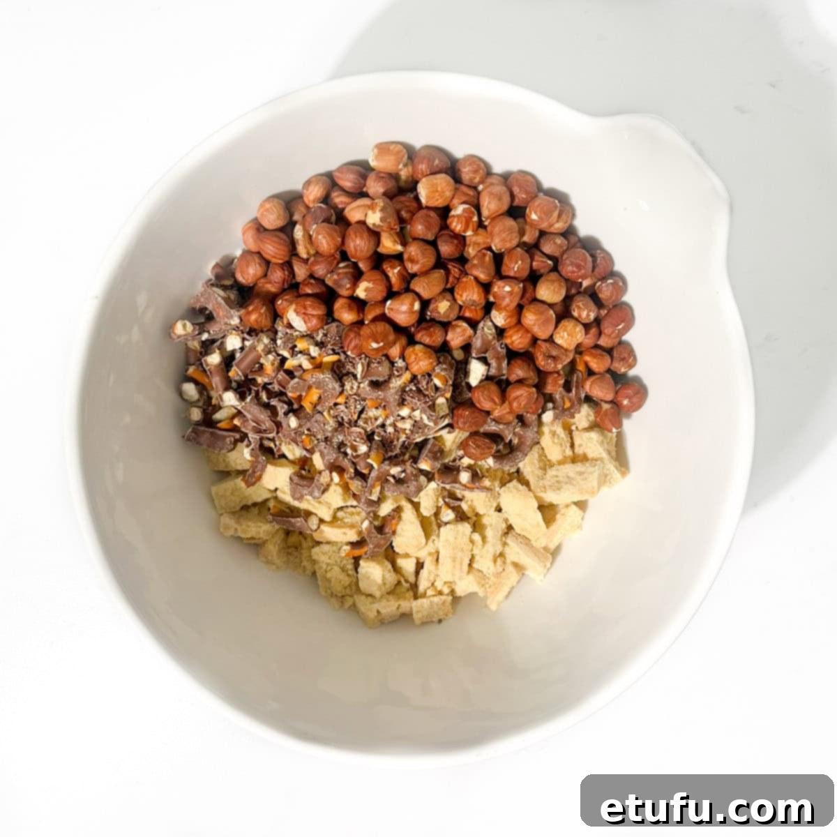 Decadent No-Bake Chocolate Biscuit Delight 7 Dry ingredients for the chocolate fridge cake, including biscuits, nuts, and pretzels, in a large white bowl.